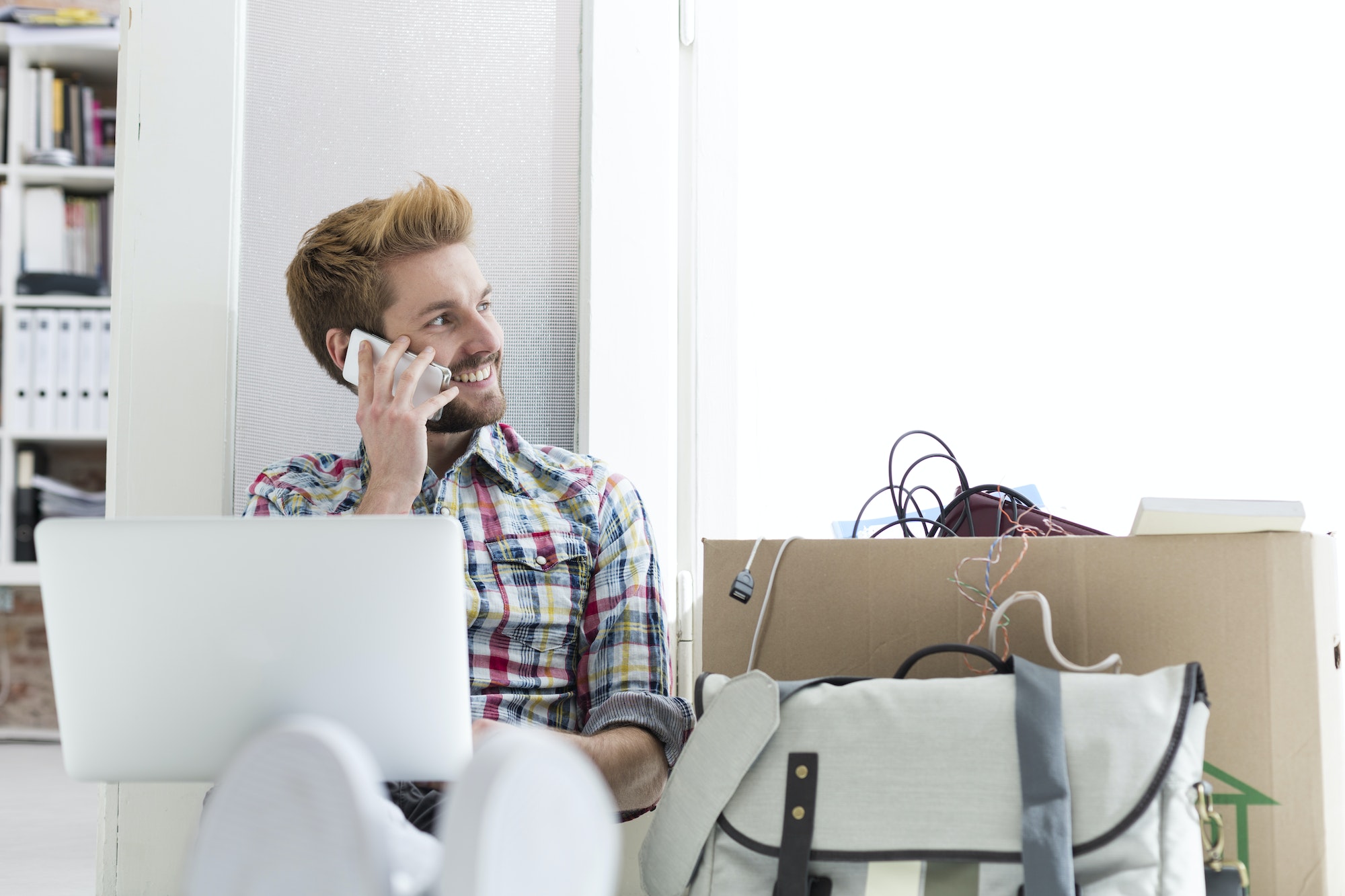 Young man sitting on floor in office using laptop and cell phone